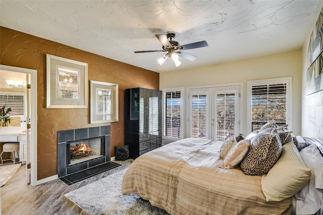 bedroom with access to exterior, ceiling fan, french doors, hardwood / wood-style floors, and a tiled fireplace