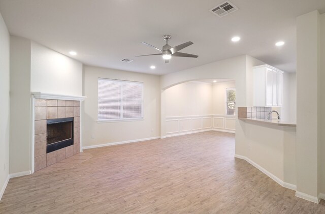 unfurnished living room featuring ceiling fan, a healthy amount of sunlight, a fireplace, and light hardwood / wood-style flooring