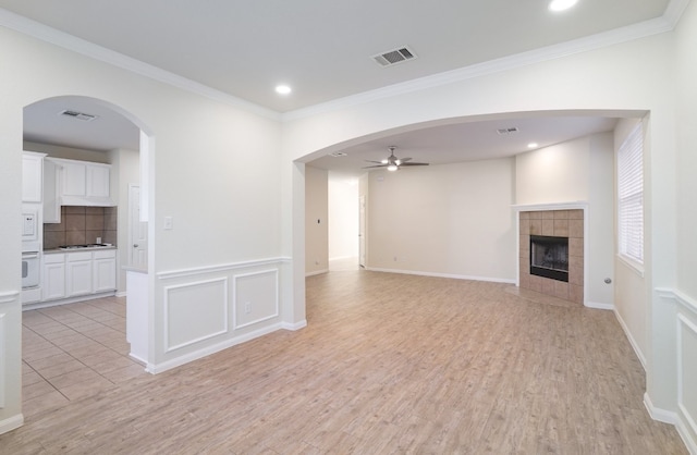 unfurnished living room with light hardwood / wood-style floors, ceiling fan, ornamental molding, and a tiled fireplace