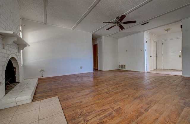 unfurnished living room with a textured ceiling, light wood-type flooring, a brick fireplace, and ceiling fan