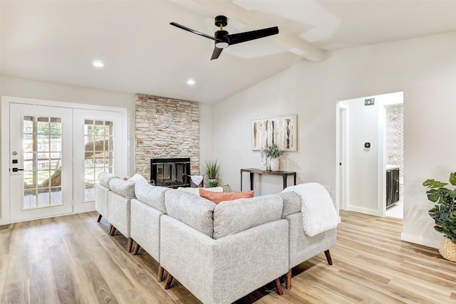 living room featuring a stone fireplace, ceiling fan, lofted ceiling with beams, and light wood-type flooring