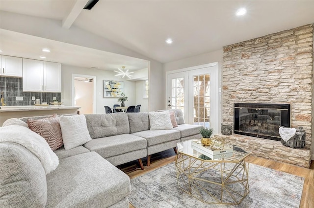 living room featuring lofted ceiling with beams, ceiling fan, a fireplace, and light hardwood / wood-style flooring