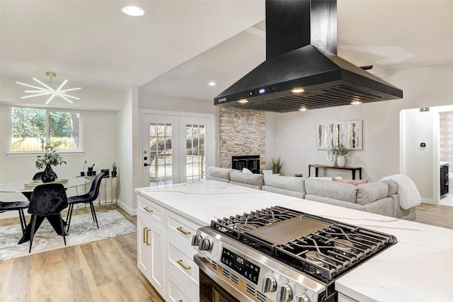 kitchen with white cabinets, wall chimney exhaust hood, light stone counters, and gas range