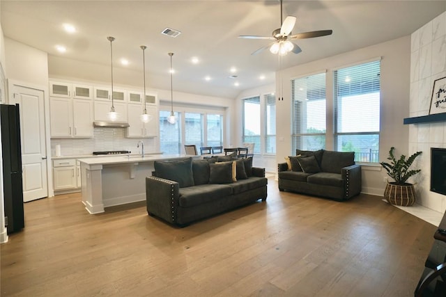 living room featuring a tile fireplace, light hardwood / wood-style floors, ceiling fan, and sink