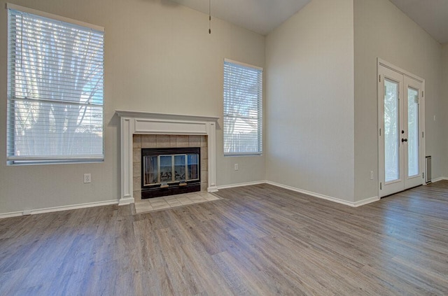 unfurnished living room featuring wood-type flooring, french doors, and a tiled fireplace