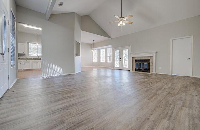 unfurnished living room with a ceiling fan, visible vents, high vaulted ceiling, light wood-style flooring, and a tiled fireplace