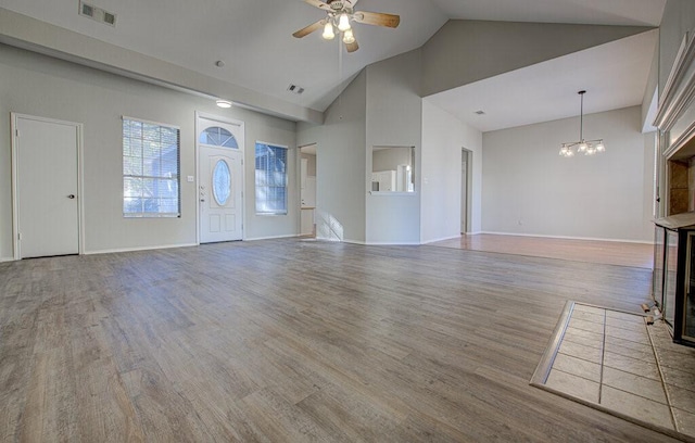 unfurnished living room with hardwood / wood-style flooring, ceiling fan with notable chandelier, a fireplace, and high vaulted ceiling