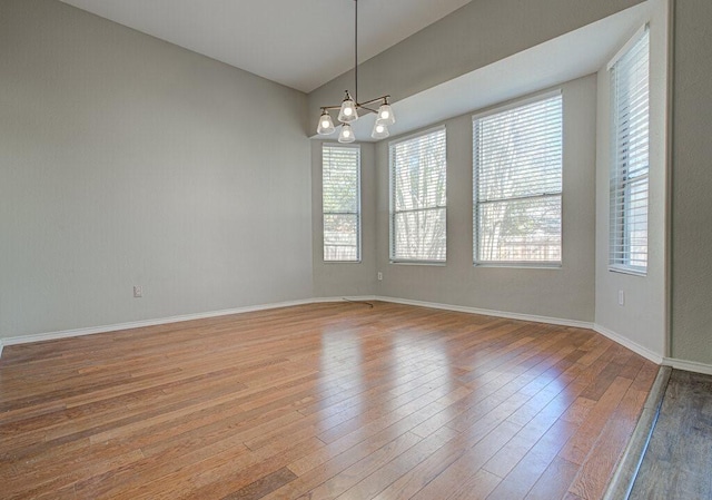 spare room featuring hardwood / wood-style flooring, a notable chandelier, baseboards, and a wealth of natural light