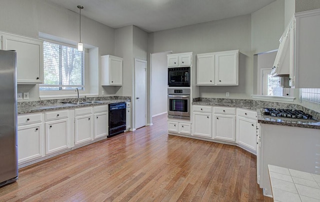 kitchen featuring black appliances, light wood-style floors, hanging light fixtures, white cabinetry, and a sink