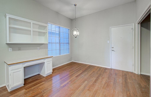 unfurnished office featuring baseboards, a notable chandelier, light wood-style flooring, and built in study area