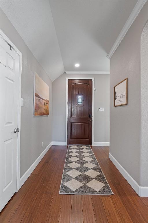 entrance foyer featuring crown molding, dark wood-type flooring, and vaulted ceiling