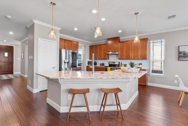 kitchen featuring dark hardwood / wood-style flooring, ornamental molding, a breakfast bar, stainless steel appliances, and an island with sink