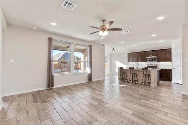 kitchen with light wood-type flooring, stainless steel appliances, ceiling fan, a breakfast bar area, and an island with sink