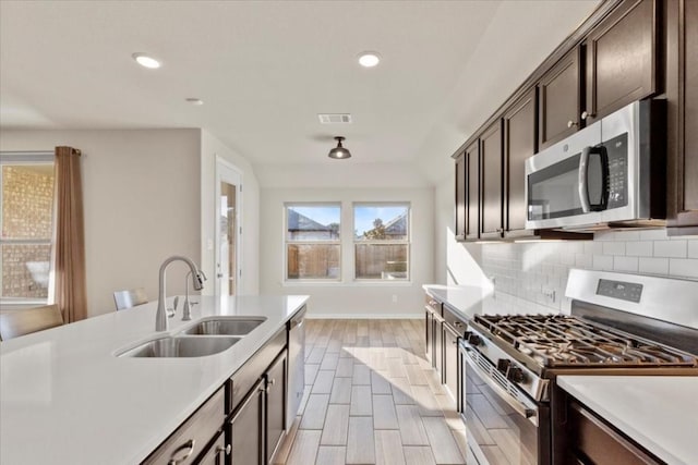 kitchen with backsplash, sink, light wood-type flooring, dark brown cabinets, and stainless steel appliances