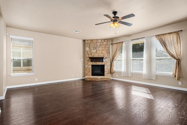 unfurnished living room with a stone fireplace, ceiling fan, and dark wood-type flooring