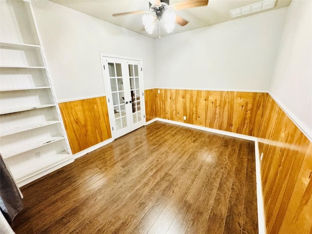 spare room with wooden walls, french doors, ceiling fan, and wood-type flooring