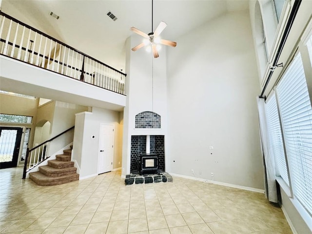 unfurnished living room with a wood stove, ceiling fan, high vaulted ceiling, and light tile patterned flooring