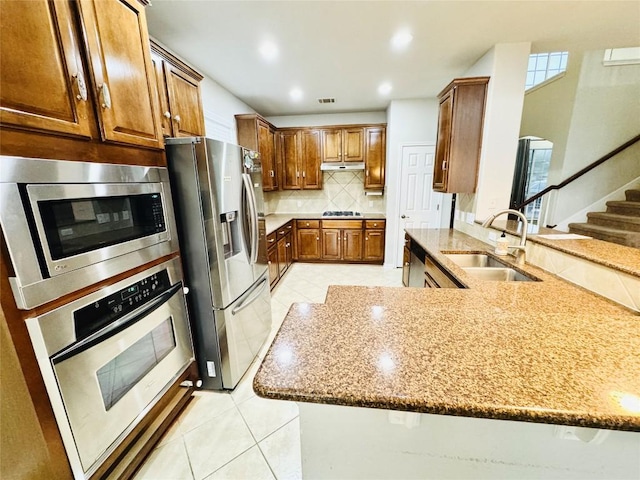 kitchen featuring sink, light stone counters, kitchen peninsula, decorative backsplash, and appliances with stainless steel finishes