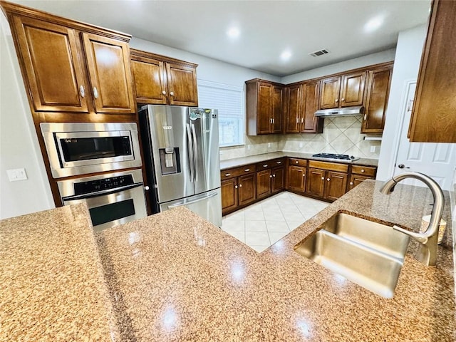 kitchen with backsplash, stainless steel appliances, light stone counters, and sink