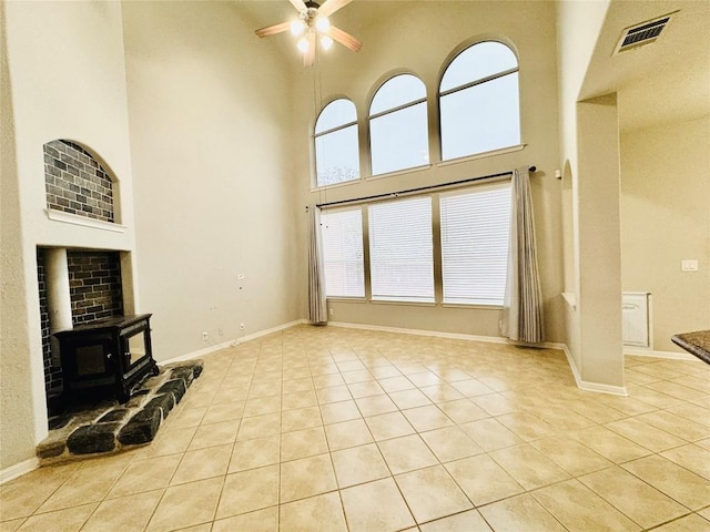 living room featuring light tile patterned floors, a towering ceiling, a wood stove, and ceiling fan