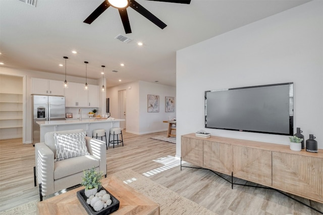 living room featuring light wood-type flooring, ceiling fan, and sink