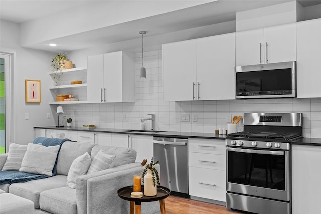 kitchen with sink, white cabinetry, light wood-type flooring, appliances with stainless steel finishes, and pendant lighting