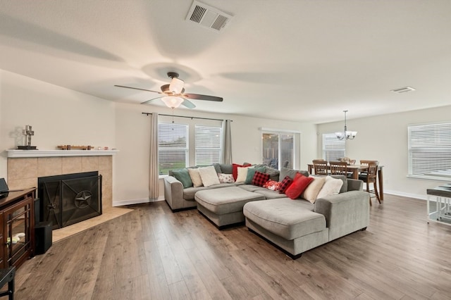 living room featuring a tile fireplace, ceiling fan with notable chandelier, and hardwood / wood-style floors