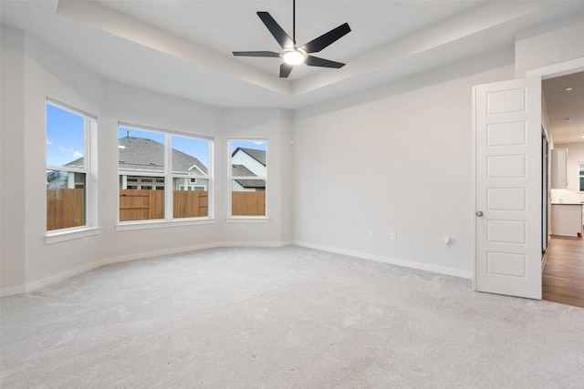 empty room with light carpet, a raised ceiling, and ceiling fan