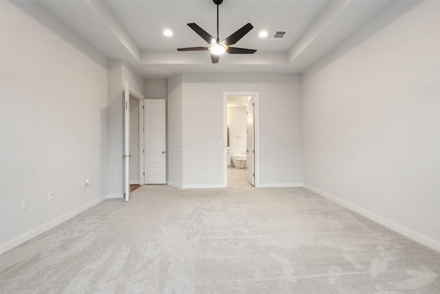 unfurnished bedroom featuring ceiling fan, light colored carpet, ensuite bathroom, and a tray ceiling