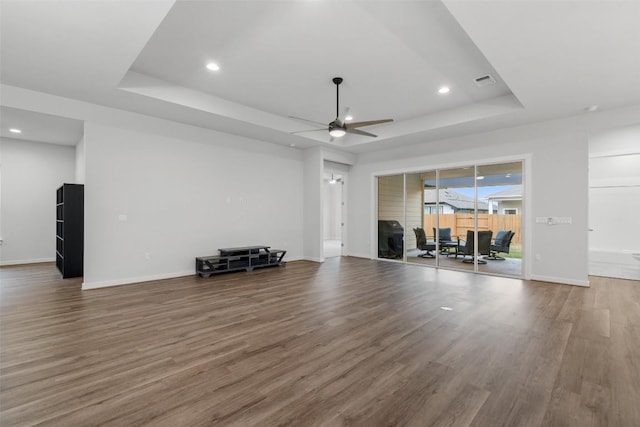 unfurnished living room with hardwood / wood-style floors, ceiling fan, and a raised ceiling