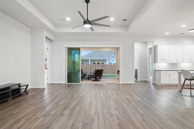 living room featuring a tray ceiling, ceiling fan, and light hardwood / wood-style flooring