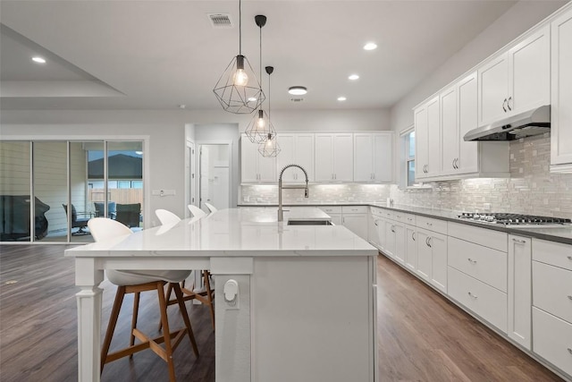 kitchen featuring light stone countertops, sink, dark wood-type flooring, hanging light fixtures, and a center island with sink