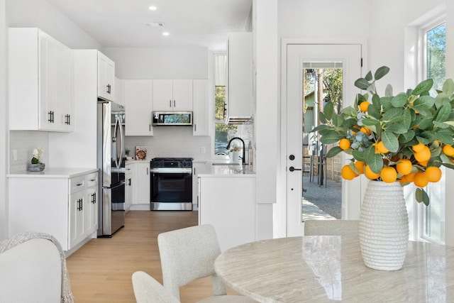 kitchen featuring light hardwood / wood-style floors, a healthy amount of sunlight, white cabinetry, and appliances with stainless steel finishes