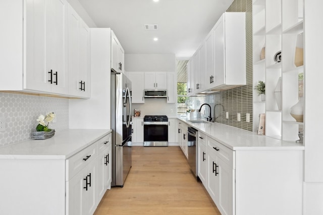 kitchen with tasteful backsplash, stainless steel appliances, sink, light hardwood / wood-style floors, and white cabinetry