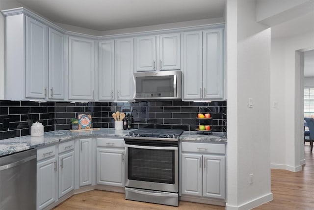 kitchen with white cabinets, light hardwood / wood-style flooring, appliances with stainless steel finishes, tasteful backsplash, and light stone counters