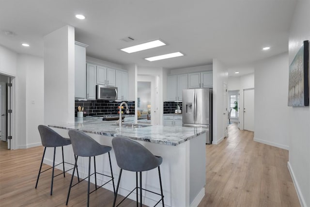 kitchen featuring kitchen peninsula, appliances with stainless steel finishes, decorative backsplash, light stone counters, and light hardwood / wood-style flooring