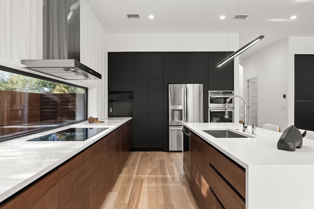 kitchen with stainless steel appliances, light hardwood / wood-style flooring, wall chimney exhaust hood, and sink