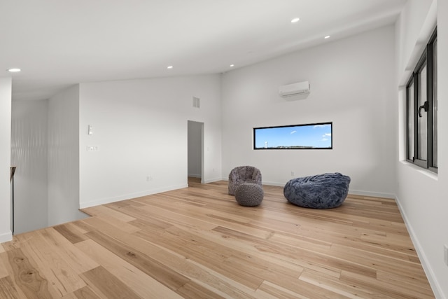 sitting room with a wall mounted air conditioner, light wood-type flooring, and high vaulted ceiling