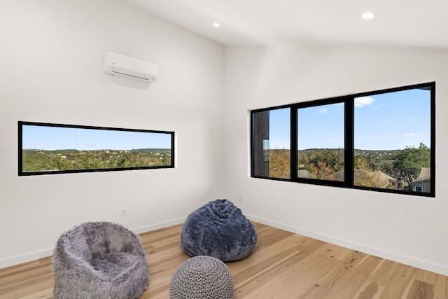 living area with an AC wall unit, lofted ceiling, and hardwood / wood-style flooring