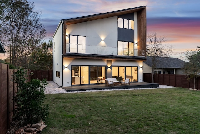 back house at dusk with outdoor lounge area, a patio area, and a lawn