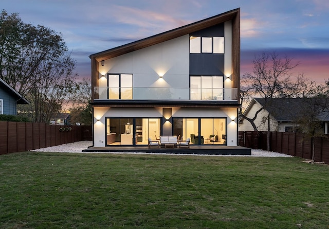 back house at dusk with an outdoor living space, a patio, a balcony, and a yard