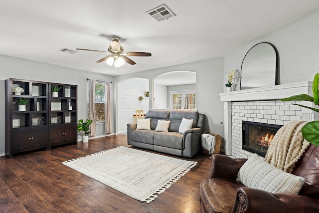 living room with ceiling fan, dark wood-type flooring, a textured ceiling, and a brick fireplace