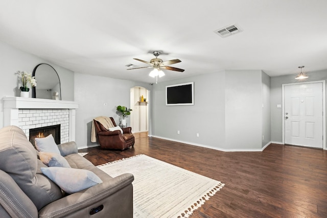 living room with ceiling fan, dark wood-type flooring, and a brick fireplace