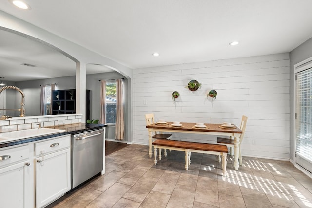 kitchen featuring stainless steel dishwasher, sink, light tile patterned floors, white cabinetry, and wood walls