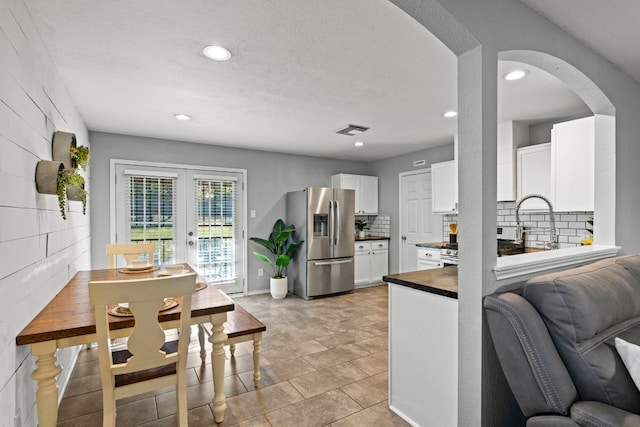 kitchen with decorative backsplash, stainless steel refrigerator with ice dispenser, white cabinetry, and french doors