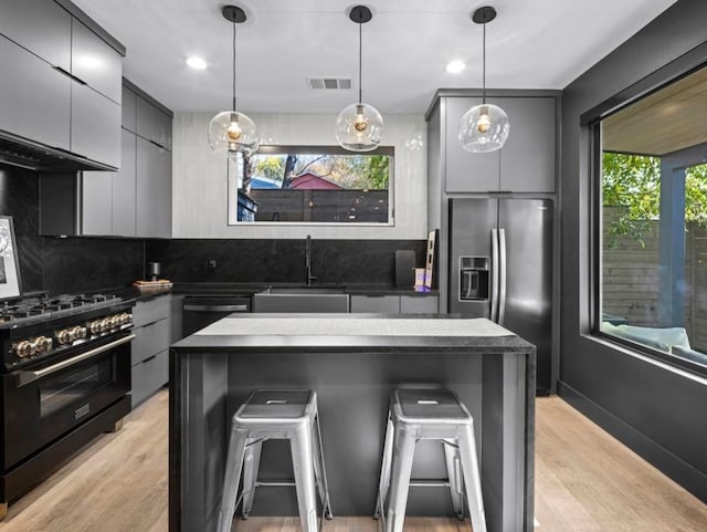 kitchen with appliances with stainless steel finishes, a kitchen breakfast bar, sink, decorative light fixtures, and a kitchen island