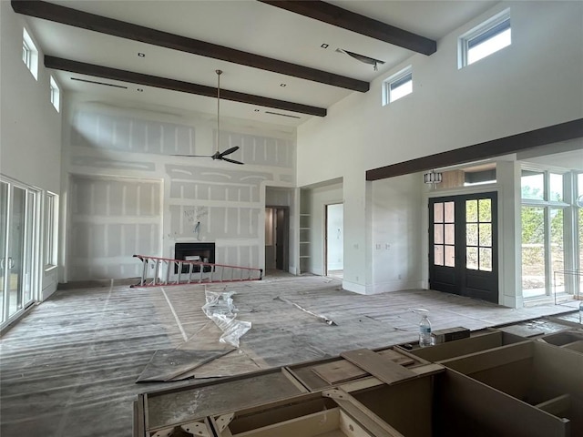 unfurnished living room with a fireplace, french doors, a ceiling fan, a towering ceiling, and beamed ceiling