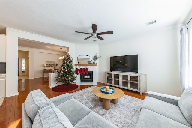 living room featuring a tiled fireplace, dark hardwood / wood-style flooring, ceiling fan with notable chandelier, and ornamental molding