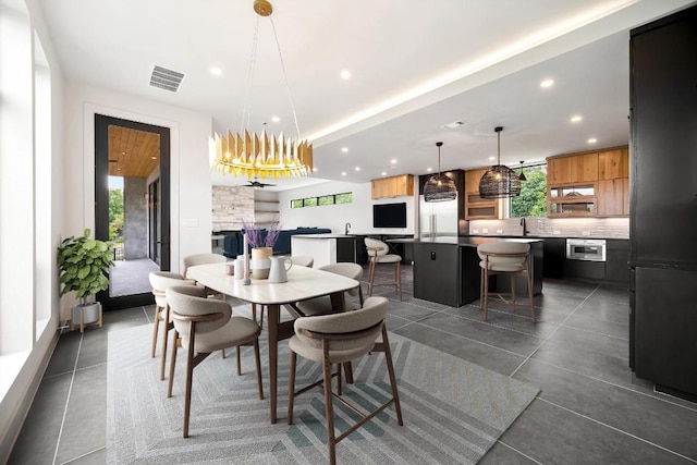 dining area with sink, a stone fireplace, a chandelier, and a healthy amount of sunlight