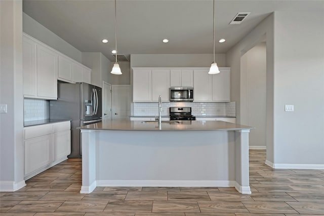 kitchen with white cabinetry, sink, stainless steel appliances, pendant lighting, and a center island with sink